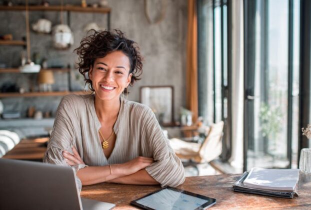 Profissional digital sorrindo e organizado em seu home office, simbolizando a organização pessoal para profissionais digitais.