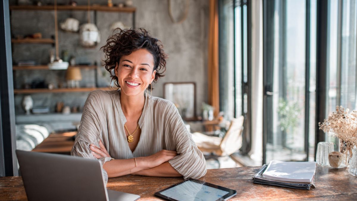 Profissional digital sorrindo e organizado em seu home office, simbolizando a organização pessoal para profissionais digitais.