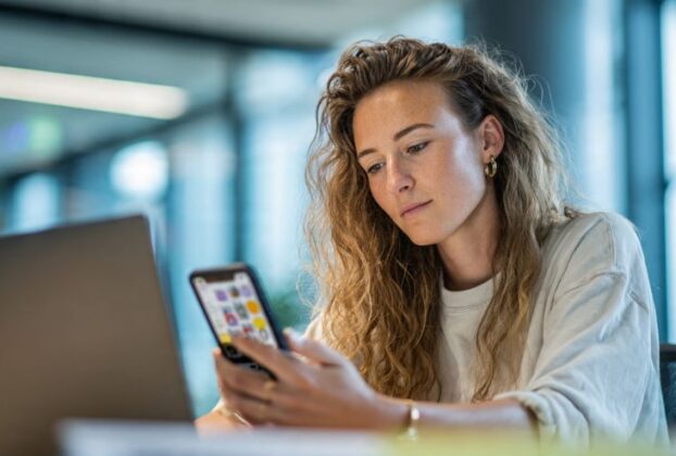 Mulher focada usando smartphone para produtividade no celular em um ambiente de trabalho moderno.