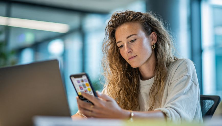 Mulher focada usando smartphone para produtividade no celular em um ambiente de trabalho moderno.
